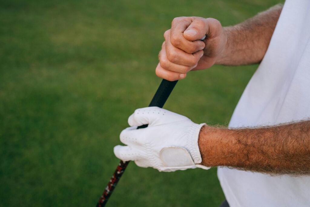 Close-up of a golfer's hands gripping a club, wearing white gloves on a green course.