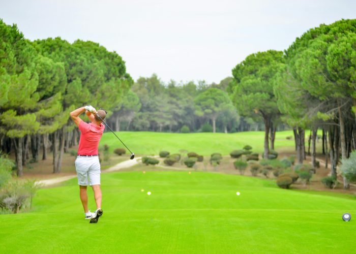 Back view of a golfer swinging a club on a lush golf course in Antalya, Türkiye.