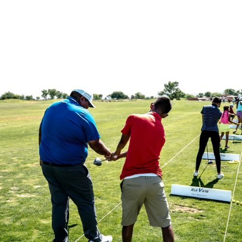 Instructor teaching golf at an outdoor course with students practicing their swings.
