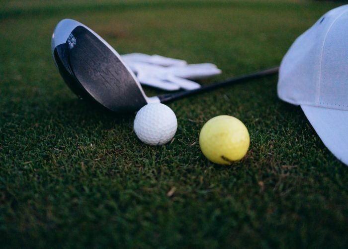 Close-up shot of a golf club, golf balls, and a cap on grass.
